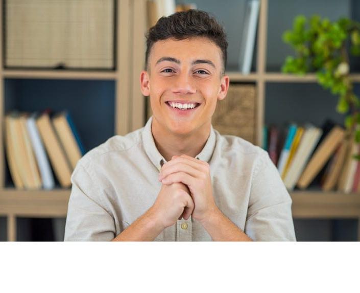 College age male looking at the camera for a portrait with books  in a shelf in backdrop